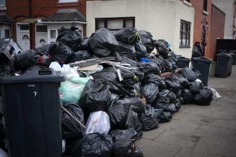 Pile of uncollected garbage bags on a residential street during a refuse workers' strike.
