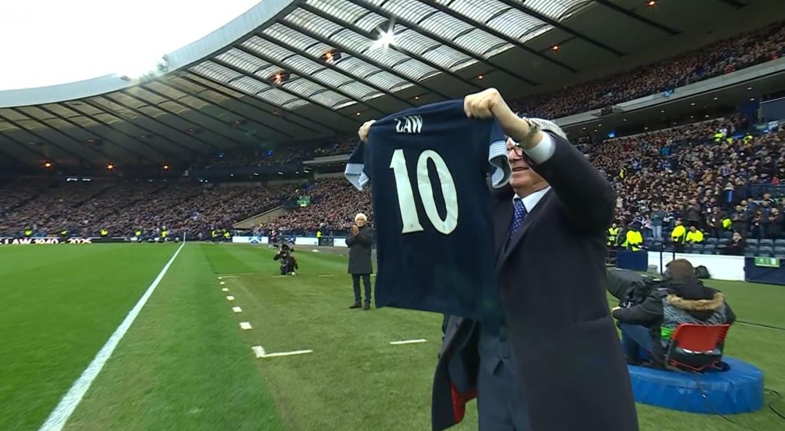 A man holding up a number 10 jersey at a soccer stadium.