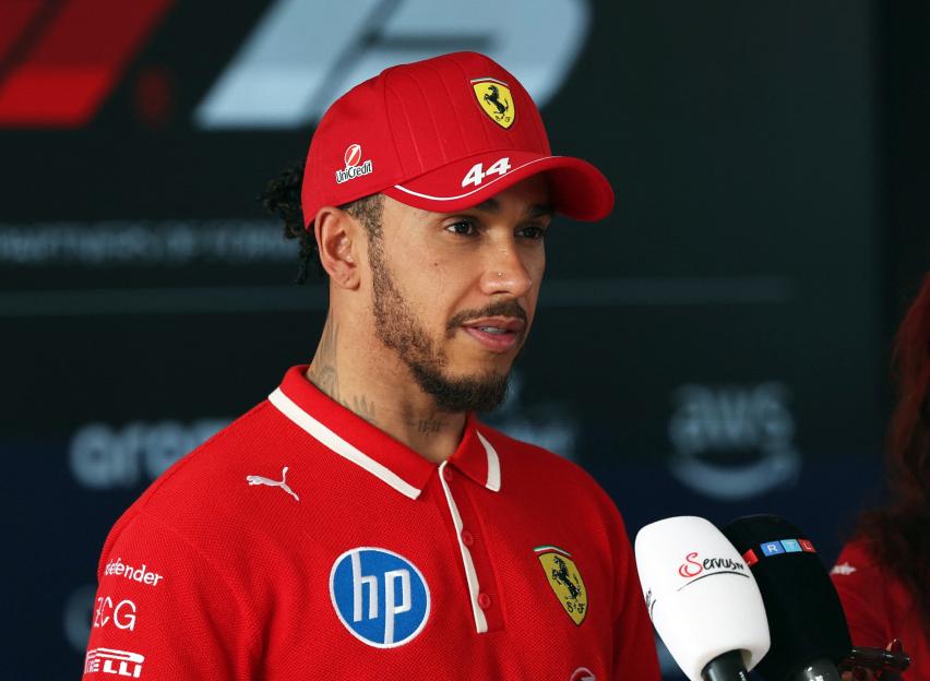 Lewis Hamilton in a Ferrari polo shirt and cap being interviewed.