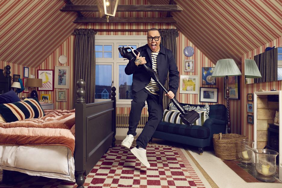 A man playfully holding a vacuum cleaner in a bedroom.