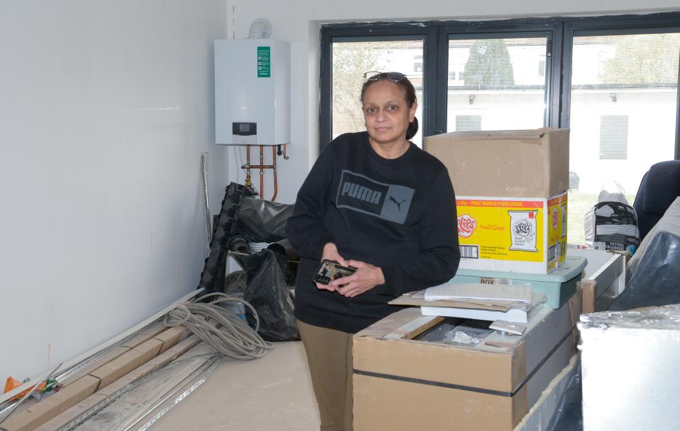 A woman stands in an unfinished room, surrounded by building materials and boxes.