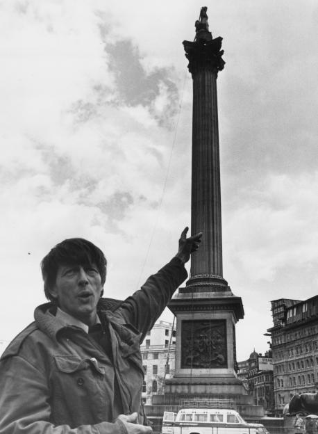 Black and white photo of John Noakes pointing to the top of Nelson's Column.