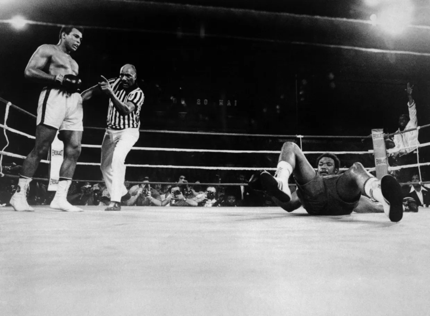 Black and white photo of a boxing match where a boxer is knocked down.