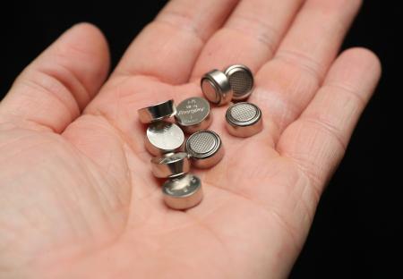 Hand holding several button batteries.