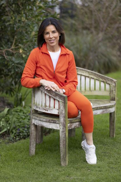 Woman in orange sportswear sitting on a weathered bench outdoors.