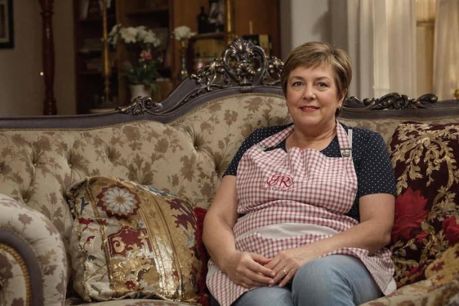 Woman in apron sitting on an ornate sofa.