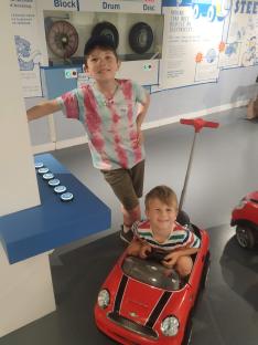 Two boys playing with toy cars in a museum exhibit about car brakes and electricity.