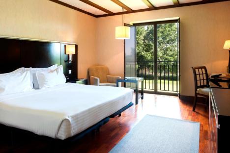 Hotel room with a bed, chair, and view of a garden.