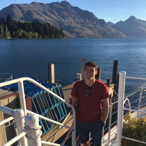 Man smiling on a boat with mountains in the background.