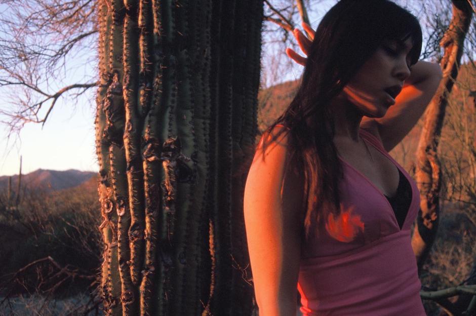 Woman standing by a saguaro cactus at sunset.