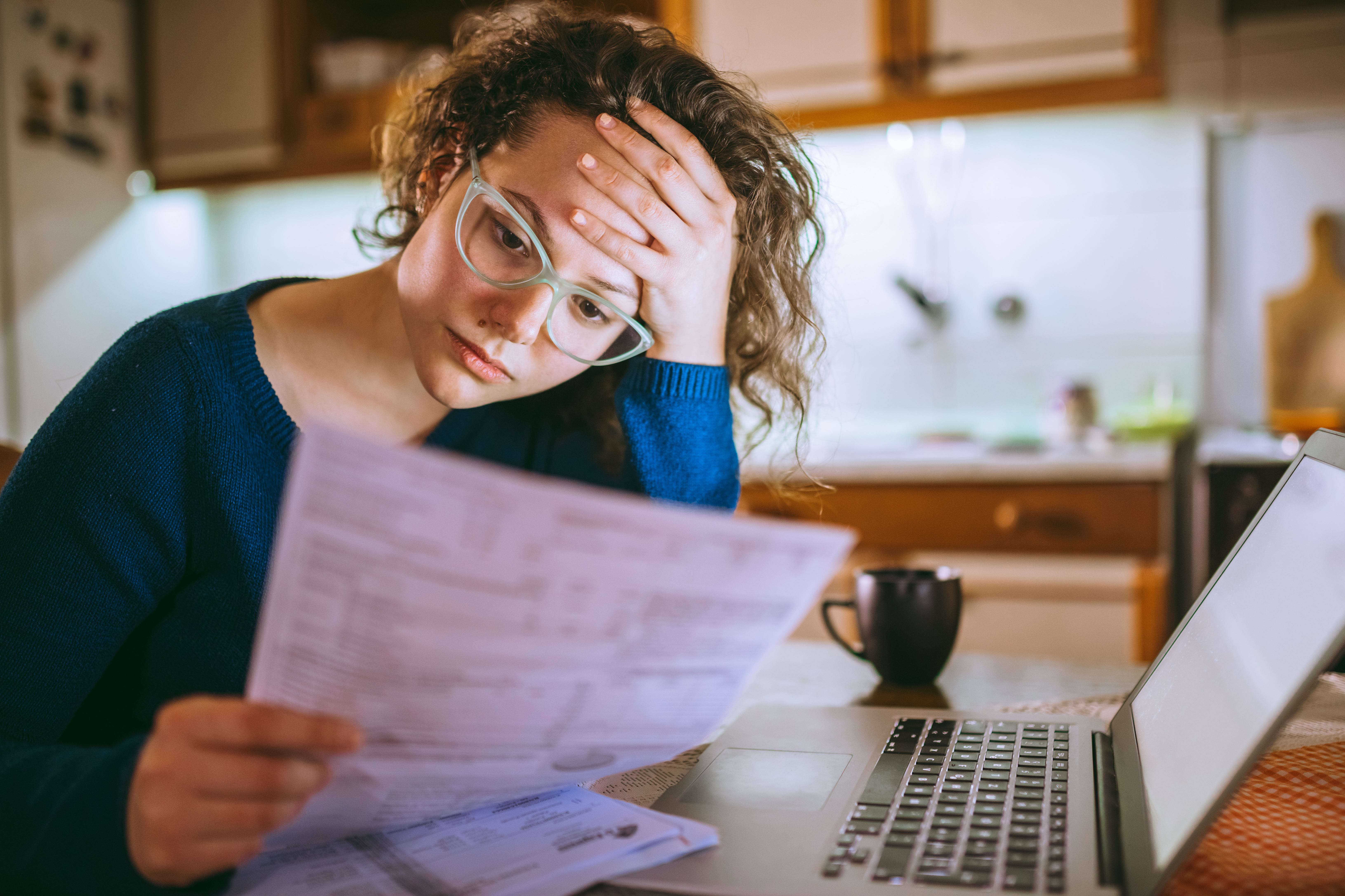 Stressed woman with laptop reading bill