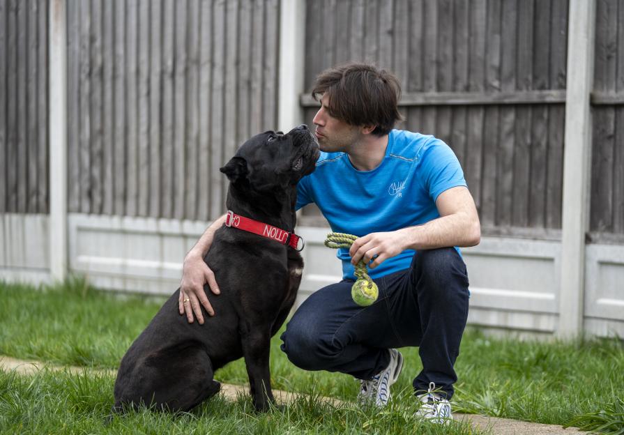 Man kneeling and kissing his black dog.