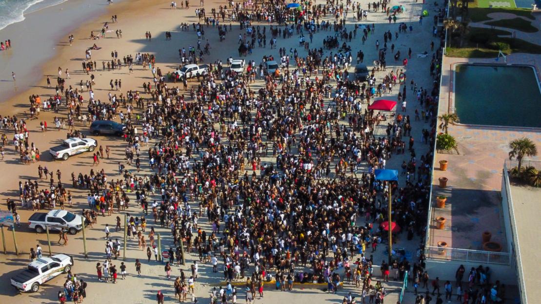 Aerial view of a large crowd on a beach with several police vehicles.