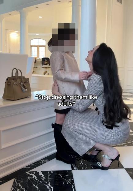 Woman holding child in expensive-looking home; text overlay reads "Stop dressing them like adults".