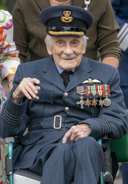 A World War II veteran in a wheelchair, wearing a military uniform and medals, waves.