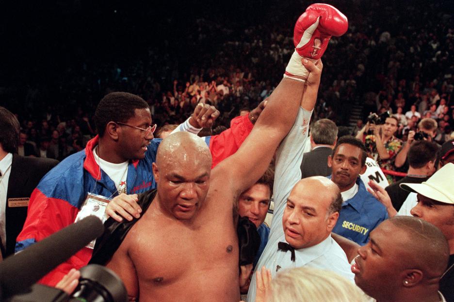 Referee raising George Foreman's arm in victory after a boxing match.