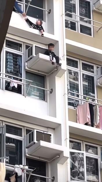 Two boys sitting on a high-rise window ledge.