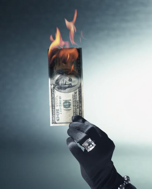 A gloved hand holding a burning $100 bill.